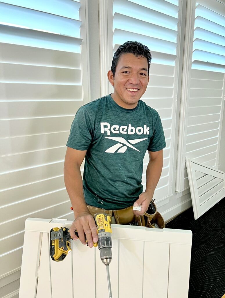 Shutter installer for Two Sisters Designs smiling and installing shutters.