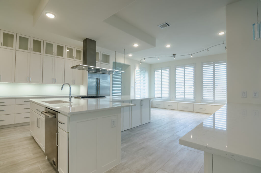 Two Sisters Designs modern kitchen in Sugar Land featuring white cabinetry, waterfall island, stainless steel hood, and full-height white plantation shutters bringing clean lines and filtered natural light to a contemporary interior.